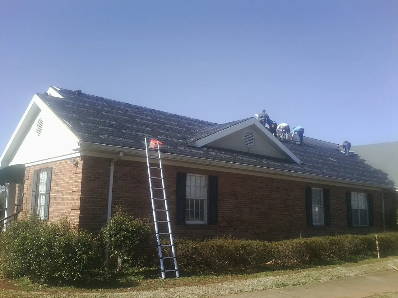 Crew tearing shingles off a brick ranch roof with a ladder set — Metal Roof Repair work by our crew in Lowpoint