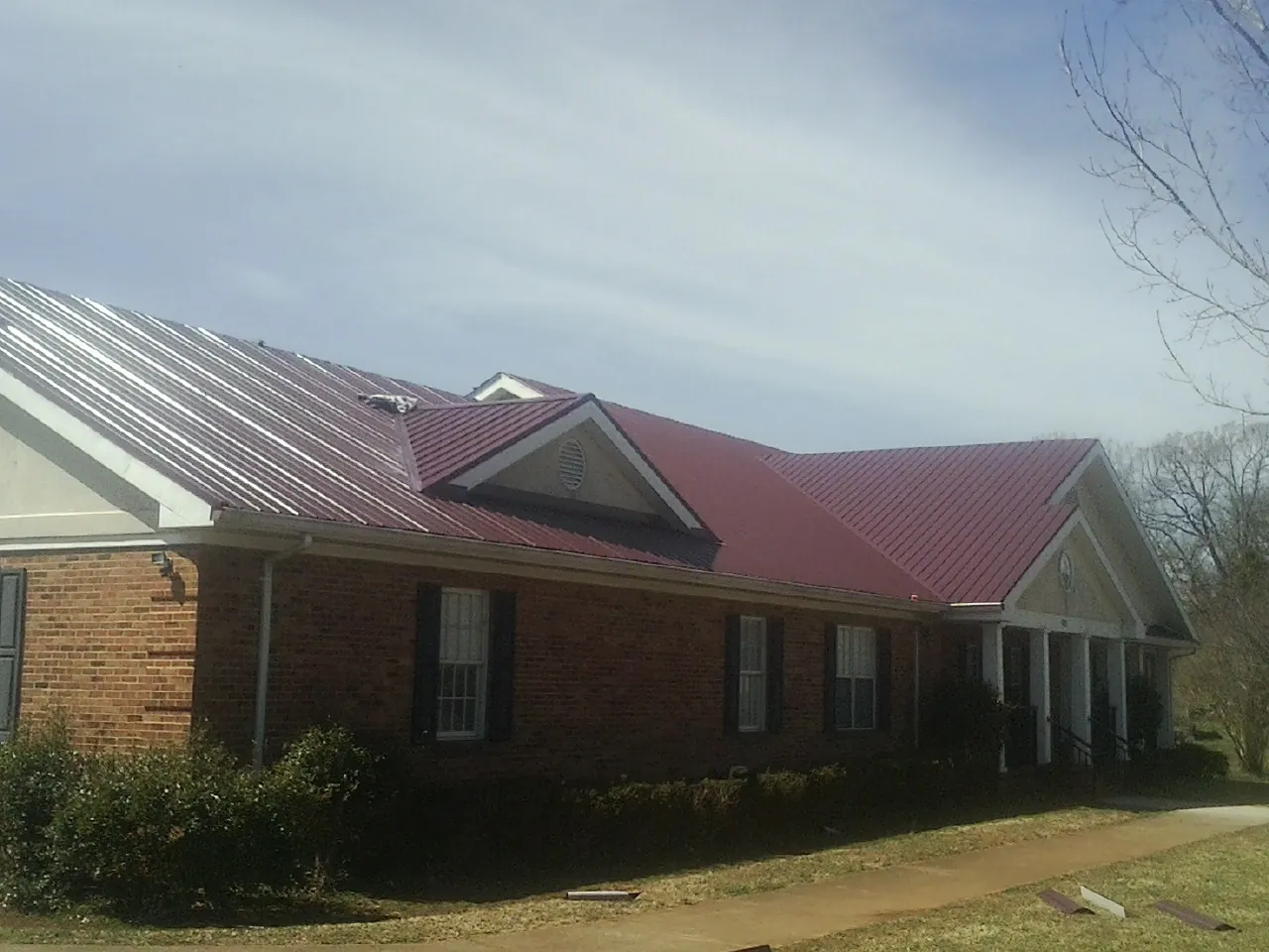 Red metal roof with gabled entries on a long brick building, from a Hail Damage Roof Repair job in Lowpoint