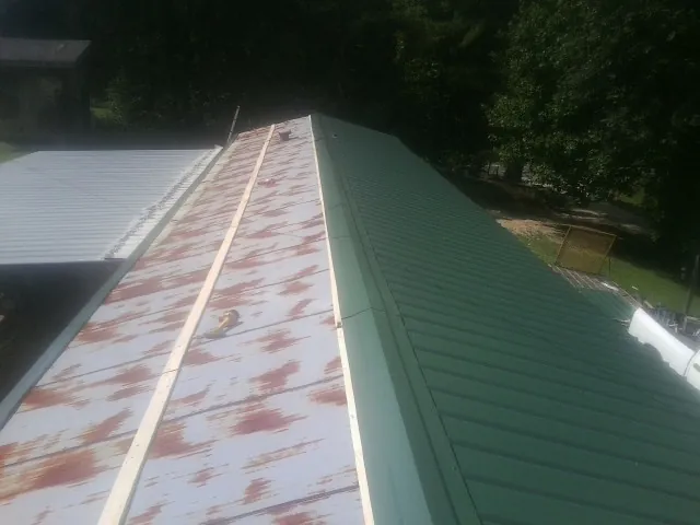Old rusted panels beside newly installed green metal roofing — Wind Damage Roof Repair by Roofing Brothers in Lowpoint