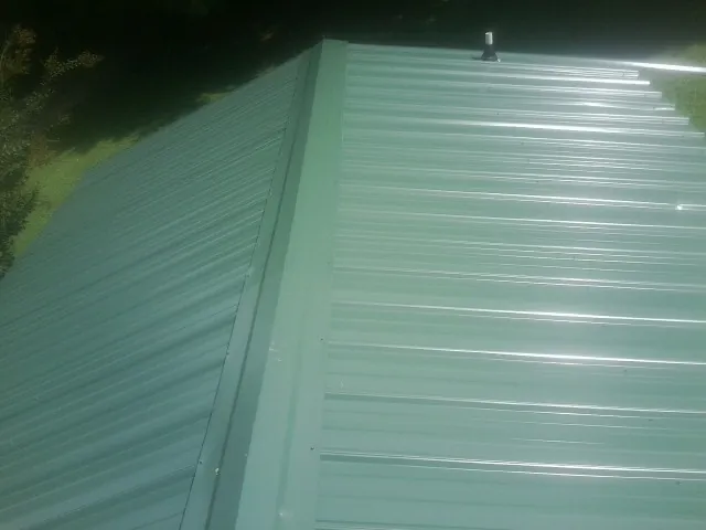 New green metal panels meeting at the ridge of a roof — Flat Roof Repair work by our crew in Lowpoint