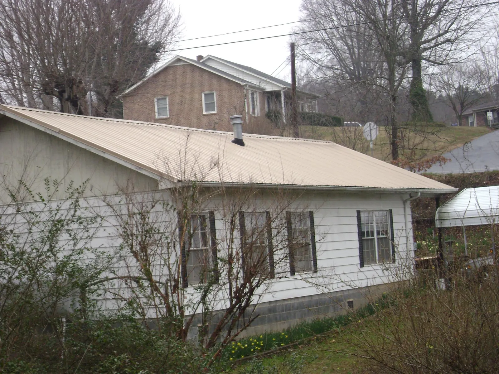 Tan metal roof on a white sided house set into a hillside — Commercial Roofing by Roofing Brothers in Lowpoint